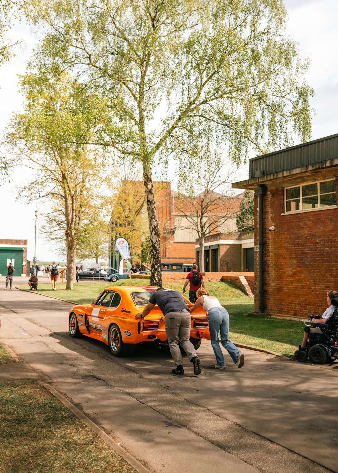 people-pushing-a-bright-orange-vintage-race-car-uhi8q5credy